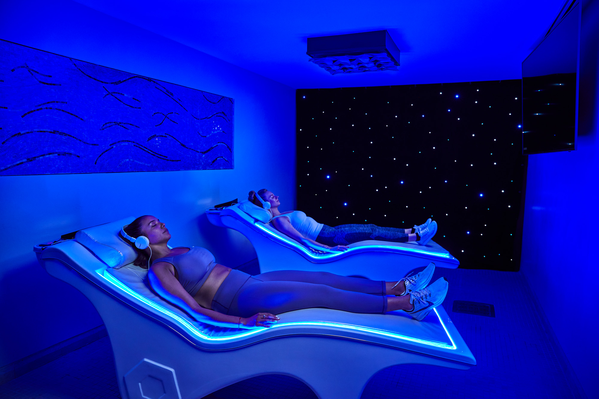 two ladies laying on a glowing infrared bed with a purple blue lit room